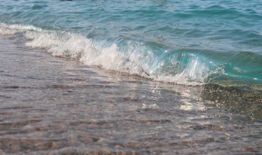 Beyaz tepeli bir deniz dalgası yükselir ve kumlu plaja çarpar. Dalga arkaplan fotoğrafı.
