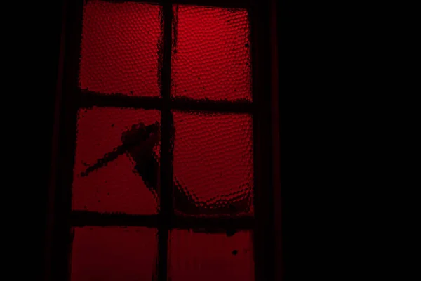 Силуэт руки с ножом видели в окне с красным светом в фоновом режиме — стоковое фото
