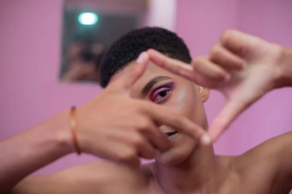 Porträt eines jungen, queeren Mannes, der durch seine Finger schaut — Stockfoto