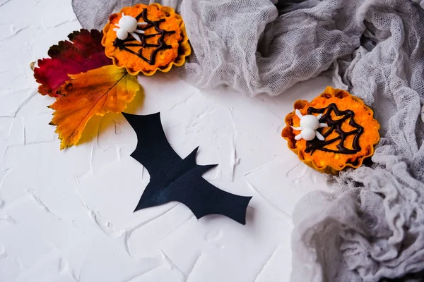Flatlay zum Thema Halloween. Orange Cupcakes auf grauem Netz auf weißem Hintergrund. es gibt eine große Fledermaus in der Nähe — Stockfoto