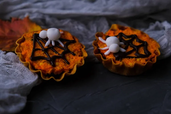 Helder oranje cupcakes in taartjes met een spin op de achtergrond van grijs web. naast herfstbladeren. concept van Halloween — Stockfoto