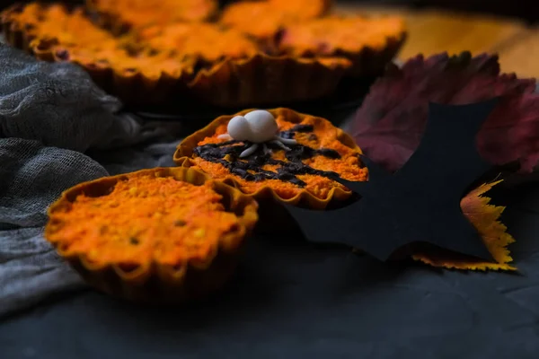 灰色の網の後ろにクモがいるタルトの明るいオレンジ色のカップケーキ。秋の紅葉の隣。ハロウィンの概念 — ストック写真