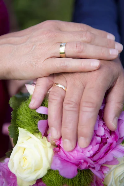Hands of bride and groom with flower bouquet — Stock Photo, Image