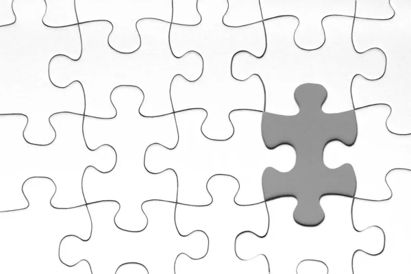 Grijze puzzel stuk in tussen van witte puzzelstukjes — Stockfoto
