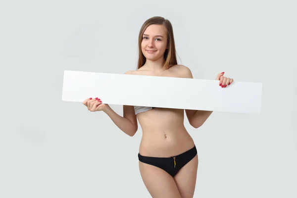 Mujer joven atractiva posando en bikini mostrando cartelera en blanco — Foto de Stock