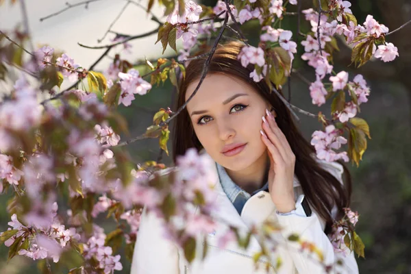 Ung flicka poserar vid busken med vårblommor — Stockfoto