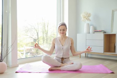 Genç ve güzel bir kadın büyük pencerenin yanında yoga yapıyor.