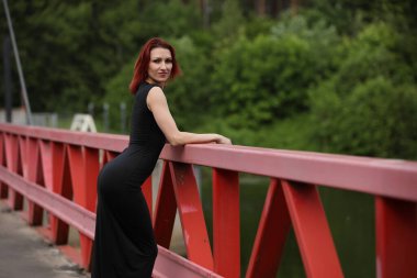 Genç stil sahibi kadın canlı kırmızı bir köprüde güven içinde poz veriyor.