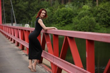 Genç stil sahibi kadın canlı kırmızı bir köprüde güven içinde poz veriyor.