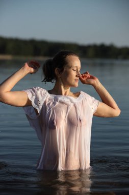 Gölde poz veren çekici kadın ıslak transparan bluz giyiyor.