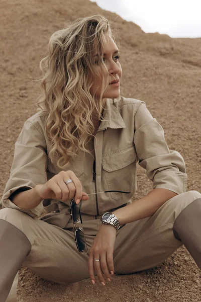 Tulumlu bir sarışın sobanın üstüne oturur ve başka tarafa bakar..