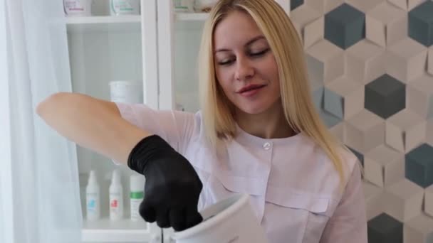 Beautiful blonde hair removal master collects wax with spatula for the procedure — Stock Video
