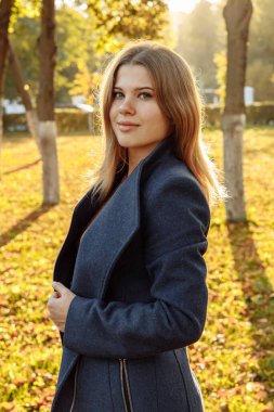 Bir sarışının fotoğrafı. Mavi ceketli genç bir kadın ılık sonbahar güneşiyle aydınlanır.