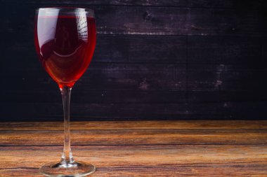 Lezzetli kırmızı şarap kadehinin fotoğrafı ahşap masa üzerinde lekeyle aydınlatılmış.