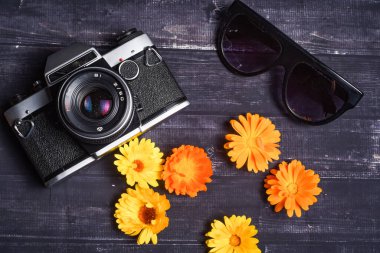 Seyahat konsepti. Yaz çiçekleri, kamera, karanlık ahşap arka planda güneş gözlüğü. Üst görünüm