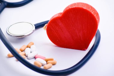 Tıbbi steteskop, haplar ve beyaz arka planda kırmızı kalp. Kardiyoloji kavramı