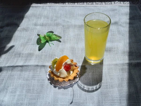 Bir turta bir sepet kremalı ve bir parça kivi ve şeftali meyveli kremalı kısa hamur işi, güneşli bir günde mavi arka planda limonatayla süslenmiş.