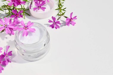 Kozmetik ve Spa prosedürleri kavramı, arka planda kremalı cam kavanoz ve pembe çiçekler. Boşluğu kopyala, kapat 