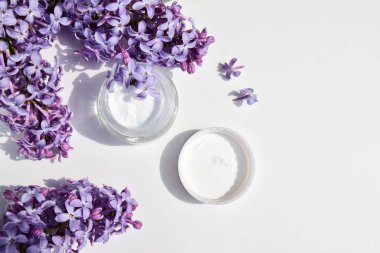 Krema için cam kavanozda kaplıca kremi, leylak çiçekli beyaz arka plan. Boşluğu kopyala.