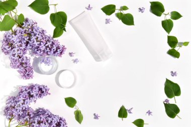 Cam kavanozda kaplıca kremi ve beyaz arka planda eflatun çiçekli ve yeşil yapraklı krema için beyaz tüp..