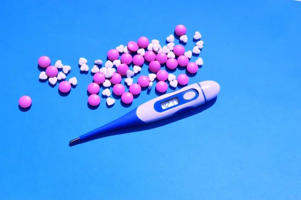 Elektronik termometre, mavi arka planda haplar veya vitaminler. Koyu mavi arka planda üst manzara. Virüslere karşı koruma, koronavirüsler, grip, soğuk algınlığı, hastalıklar. Sağlık kavramı.