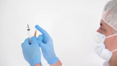 Tıbbi maskeli bir doktor elinde şırınga ve aşı ampulü tutuyor.