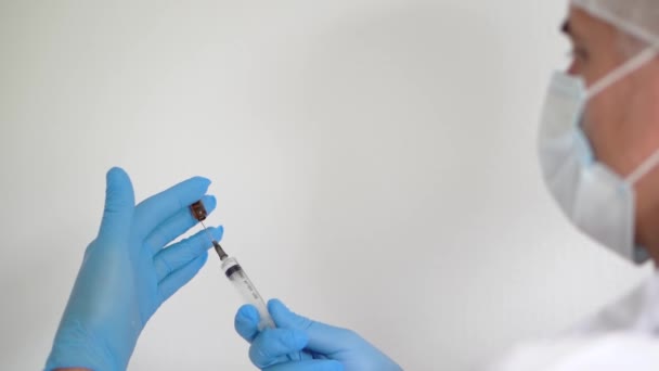 Ένας γιατρός με ιατρική μάσκα και γάντια γεμίζει ένα εμβόλιο σε μια σύριγγα, αντιγράφει χώρο — Αρχείο Βίντεο