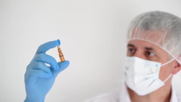 Médico en una máscara médica y guantes examina una ampolla de vacuna, espacio para copiar — Vídeo de stock