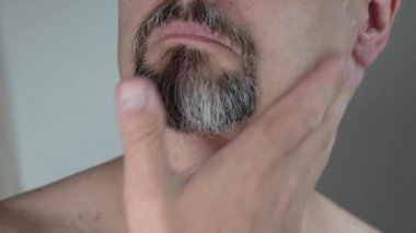 Orta yaşlı bir adam yüzüne tıraş kremi sürer. Yakın plan, 4K.