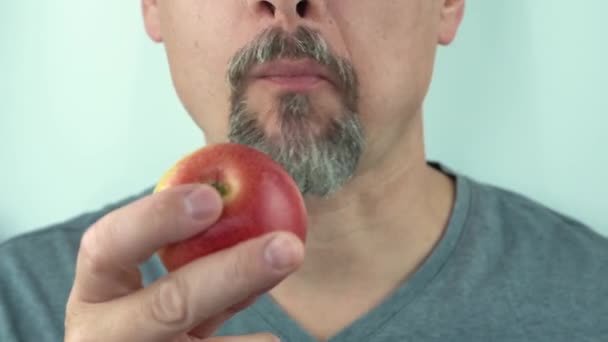 Um homem de meia idade com barba e bigode comendo uma maçã vermelha, close-up, 4K — Vídeo de Stock