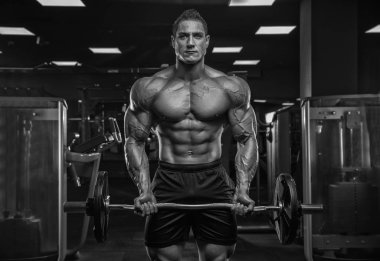 Erkek atlet vücut geliştirici halterci, modern bir spor salonunda, karanlık bir arka plana karşı, kameranın önünde poz veriyor..