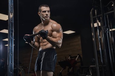 Bir genç yakışıklı vücut geliştirmeci salonunda bir egzersiz yapıyor.