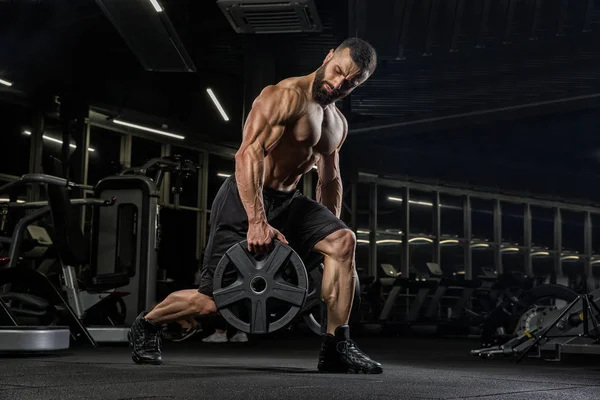 Attractive tall muscular bodybuilder doing heavy deadlifts in moder fitness center.