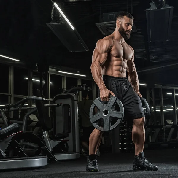 Attractive tall muscular bodybuilder doing heavy deadlifts in moder fitness center.