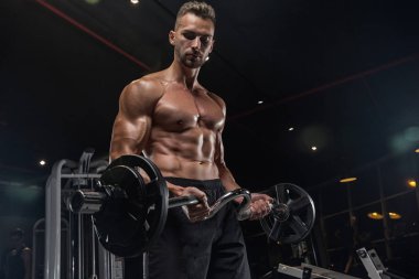 Kaslı vücut geliştirmeci adam spor salonunda dumbbells ile yapıyor