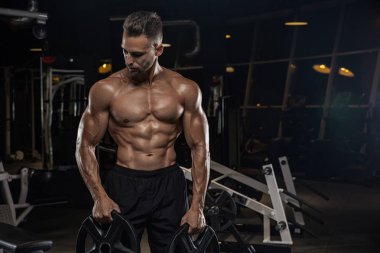 Kaslı vücut geliştirmeci adam spor salonunda dumbbells ile yapıyor