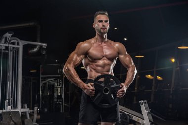 Kaslı vücut geliştirmeci adam spor salonunda dumbbells ile yapıyor