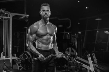 Kaslı vücut geliştirmeci adam spor salonunda dumbbells ile yapıyor