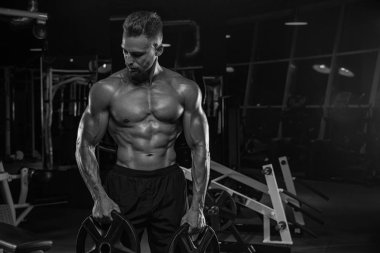 Kaslı vücut geliştirmeci adam spor salonunda dumbbells ile yapıyor