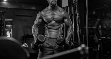 Yakışıklı ve kaslı bir adam, spor salonunda kameraya poz veriyor. 