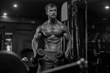 Yakışıklı ve kaslı bir adam, spor salonunda kameraya poz veriyor. 