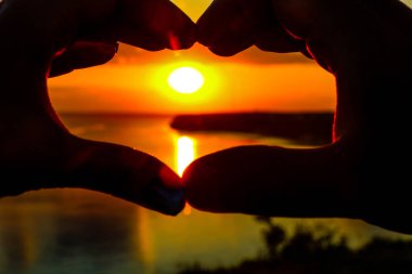 Eller günbatımına karşı kalbin şeklini gösterir.