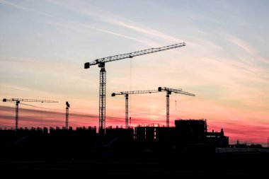 Güzel, kızıl bir günbatımının arka planında inşaat vinçleri. İyi akşamlar, inşaat..