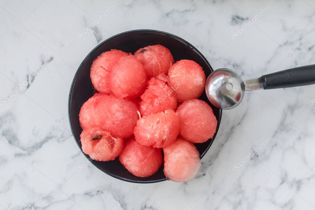 Watermelon balls, cut with a fruit spoon, in a black bowl stands on the table. Beautiful serving of fruit.