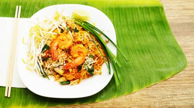  Tayland usulü kızarmış erişte, muz yaprağında beyaz tabakta karides.