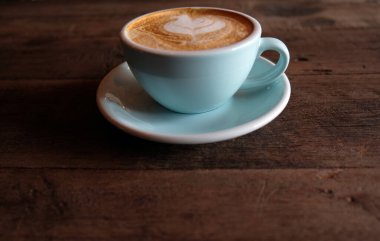 Kapuçino ya da köpüklü latte, ahşap kahve dükkanının arka planında mavi kahve bardağı.