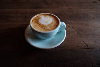 Kapuçino ya da köpüklü latte, ahşap kahve dükkanının arka planında mavi kahve bardağı.