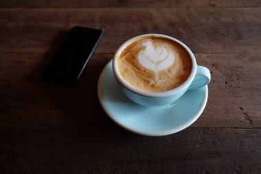 Kapuçino ya da köpüklü latte, ahşap kahve dükkanının arka planında mavi kahve bardağı.