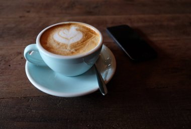 Kapuçino ya da köpüklü latte, ahşap kahve dükkanının arka planında mavi kahve bardağı.