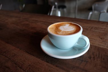 Kapuçino ya da köpüklü latte, ahşap kahve dükkanının arka planında mavi kahve bardağı.